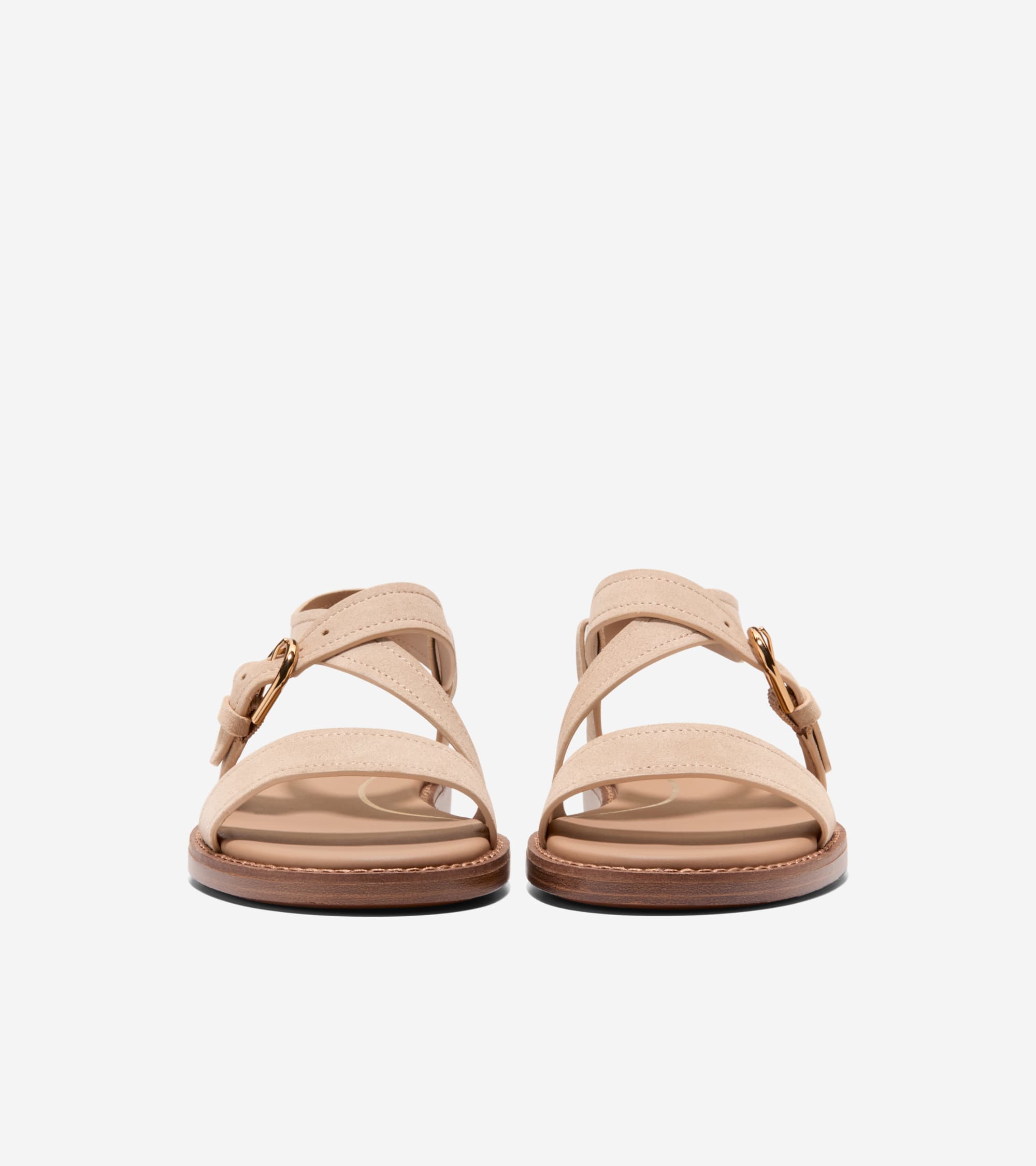 Pair of light beige suede flat sandals with crisscross straps and gold-toned buckles. Dark brown sole edge.
