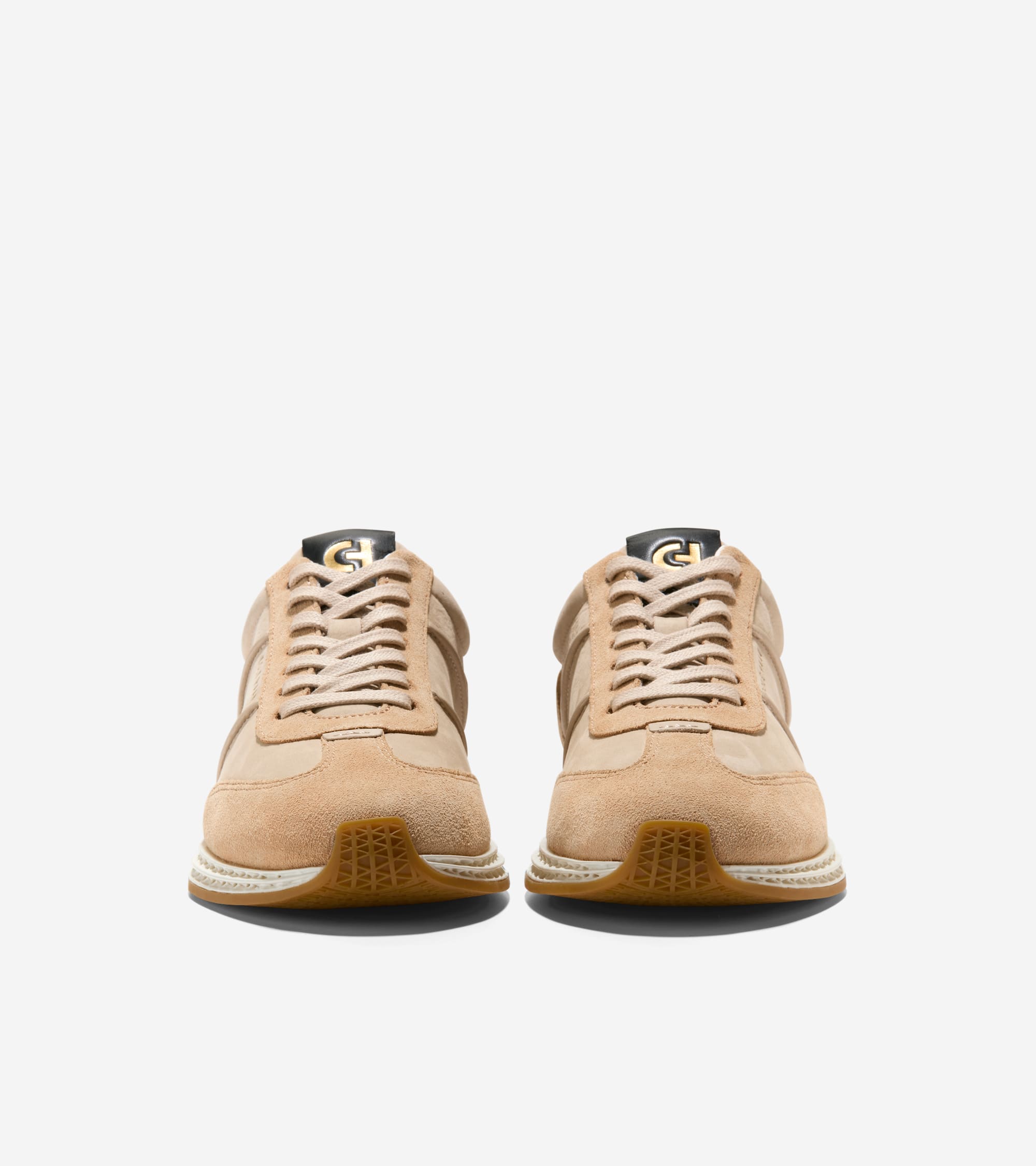Pair of tan low-profile sneakers with light tan laces, white midsoles, brown textured outsoles, and a black tongue patch with