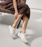 White slip-on sneakers with beige suede overlays, brown heel collars, white laces, and a white and brown sole.