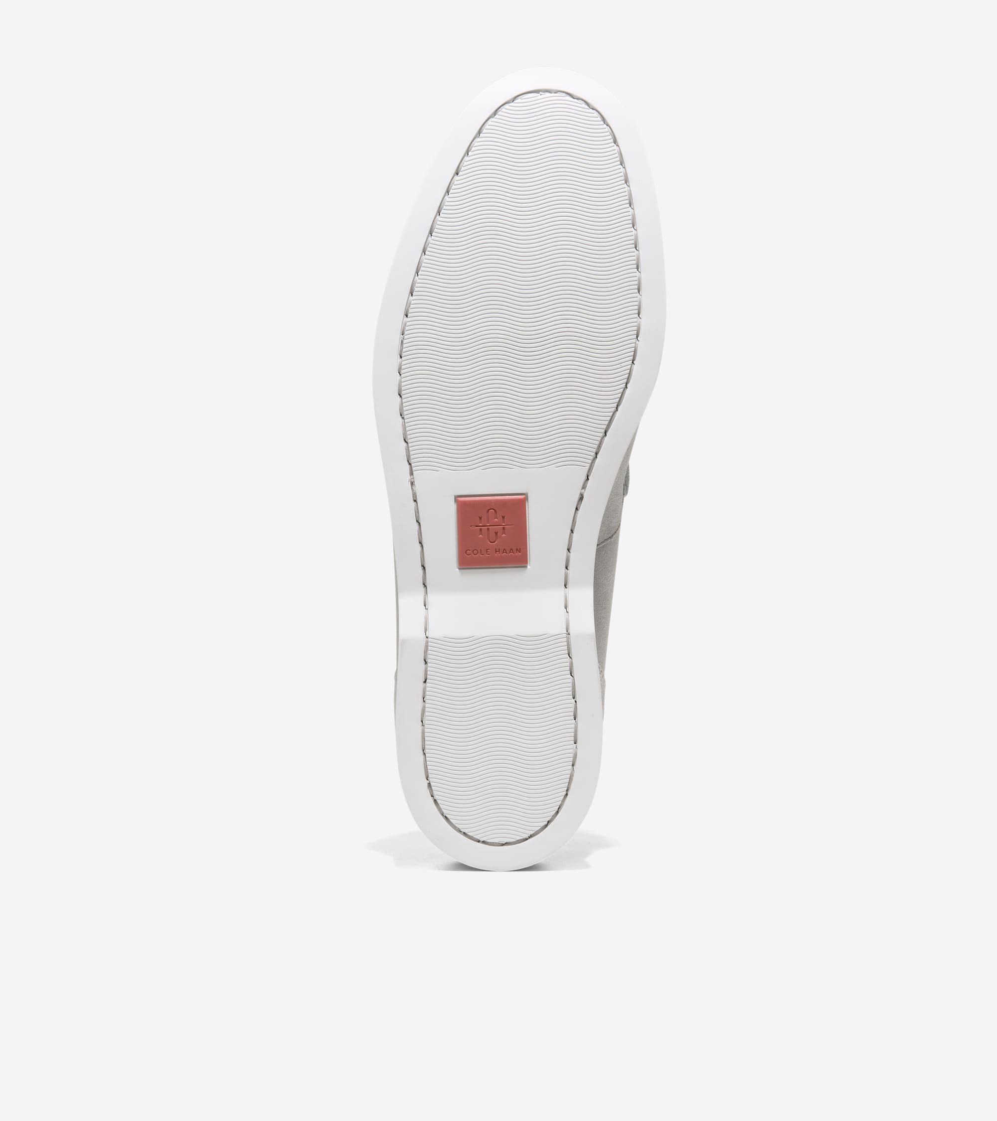 White rubber sole of a loafer with wavy texture and a reddish-brown Cole Haan logo patch near the heel.