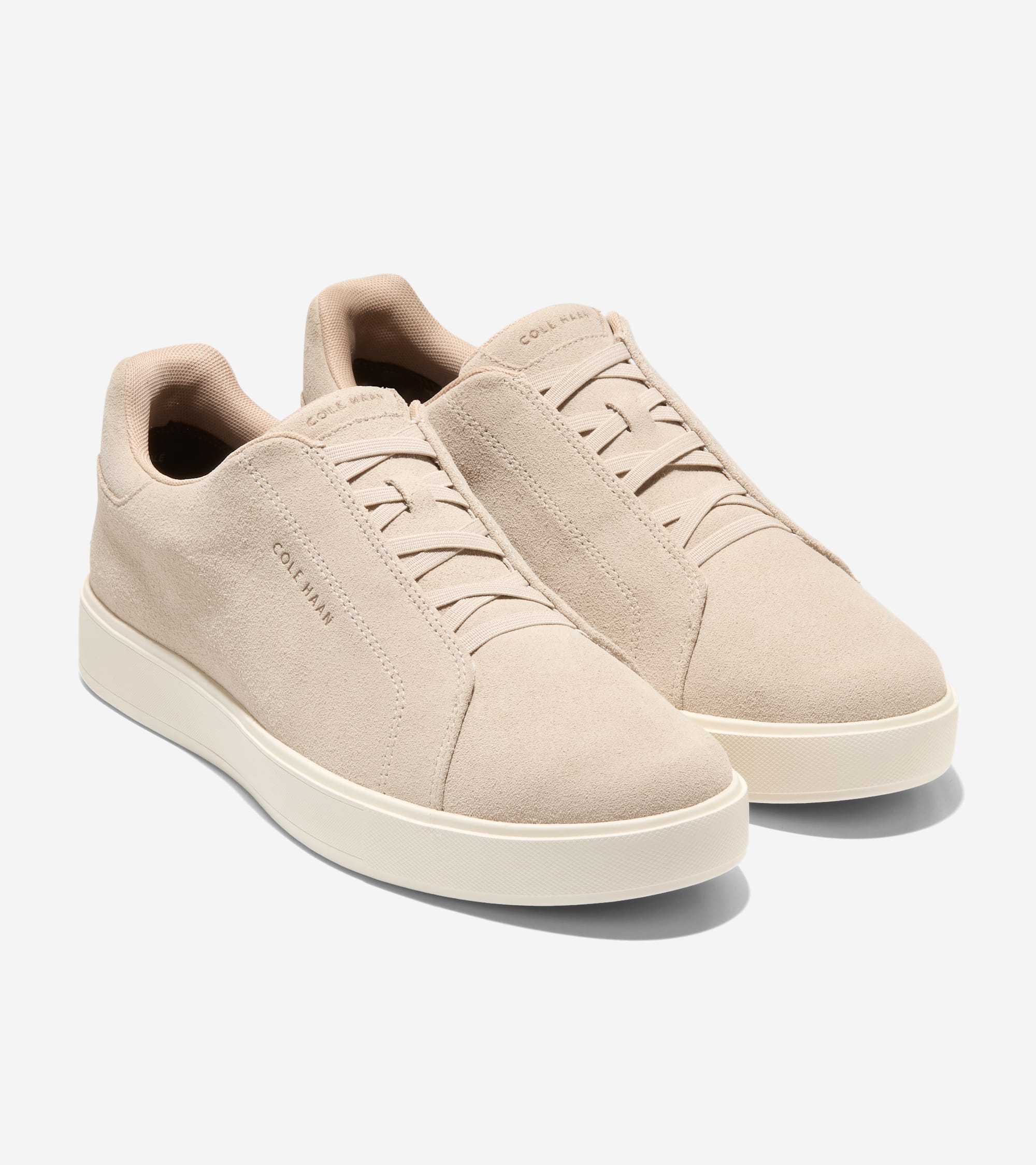 Pair of light beige suede Cole Haan slip-on sneakers with decorative elastic laces, a padded collar, and thick off-white rubb