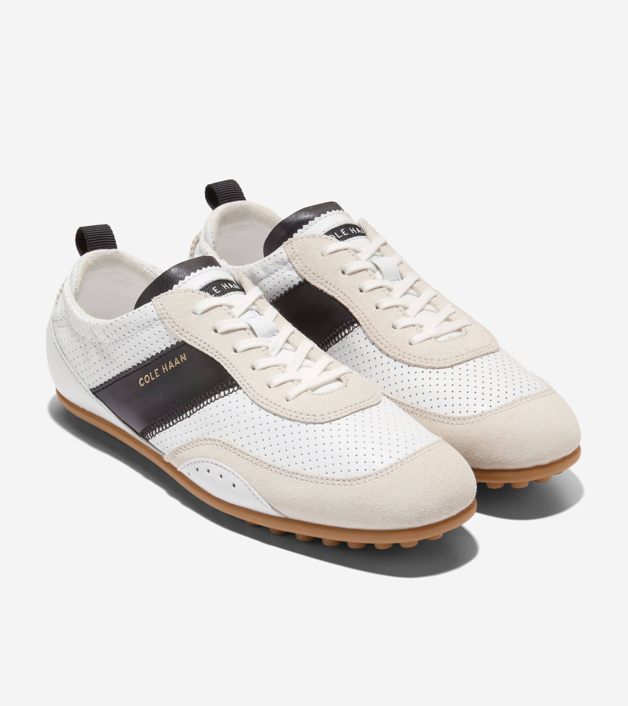 White perforated sneakers with light beige suede accents, black side stripes featuring 'COLE HAAN' text, white laces, and bro