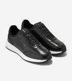 Pair of black leather slip-on sneakers with elastic laces, gold-toned Cole Haan text, and thick white soles.