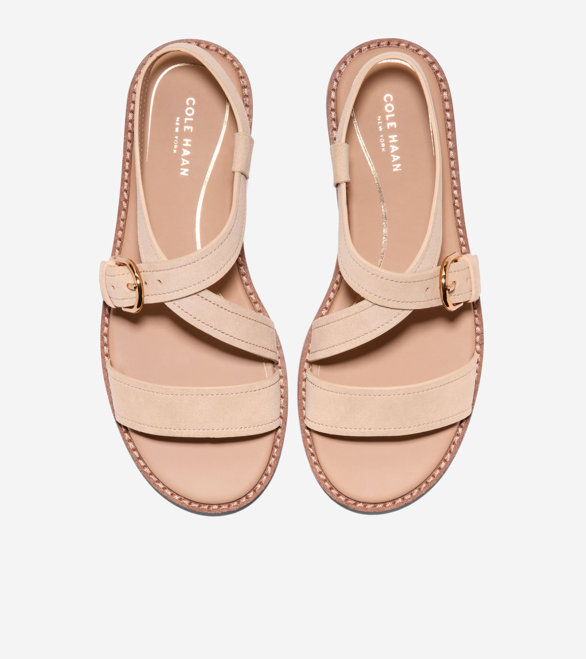 Beige flat sandals with wide toe straps, criss-cross midfoot straps, and an ankle strap with a gold-toned buckle. Stitched so
