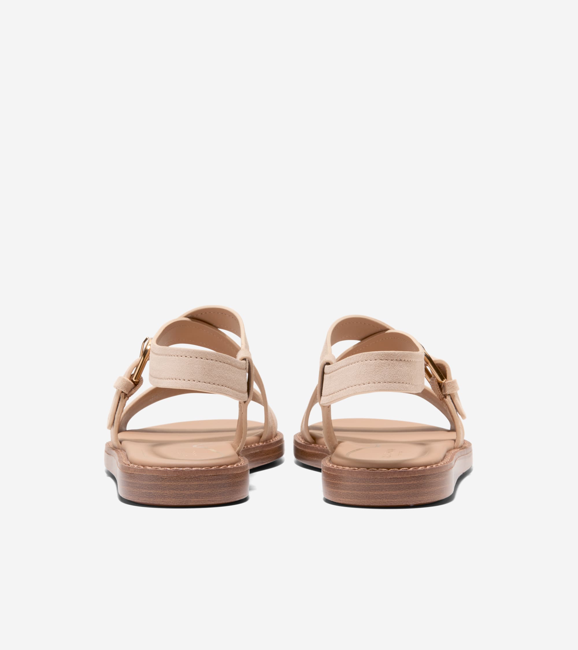 Beige suede flat sandals with wide ankle straps, gold-toned buckles, and wood-toned soles, viewed from the back.