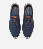Navy blue knit slip-on sneakers with tan leather collar trim, faux lacing, and off-white soles. Cole Haan branding on insole.