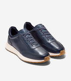 Pair of navy leather sneakers with matching laces, white midsoles, and brown textured outsoles. 'Cole Haan' on side, 'CH' log