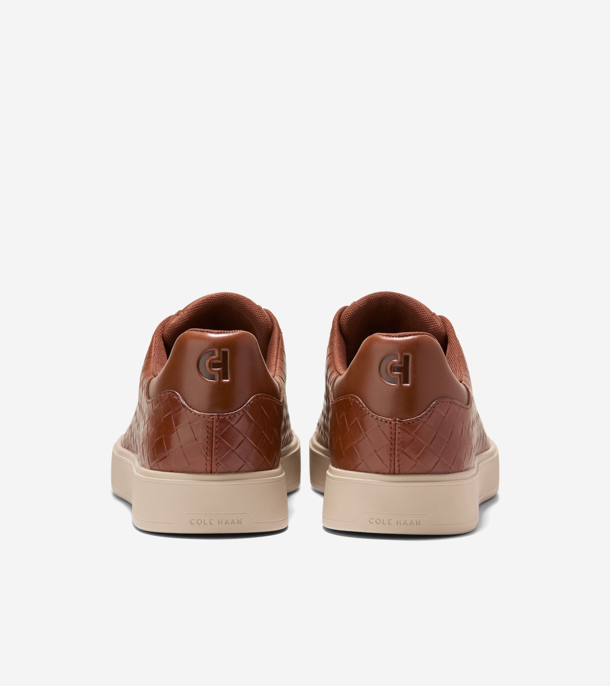 Pair of brown slip-on sneakers with woven uppers, smooth heel collars, embossed 'CH' logos, and light tan soles with 'COLE HA
