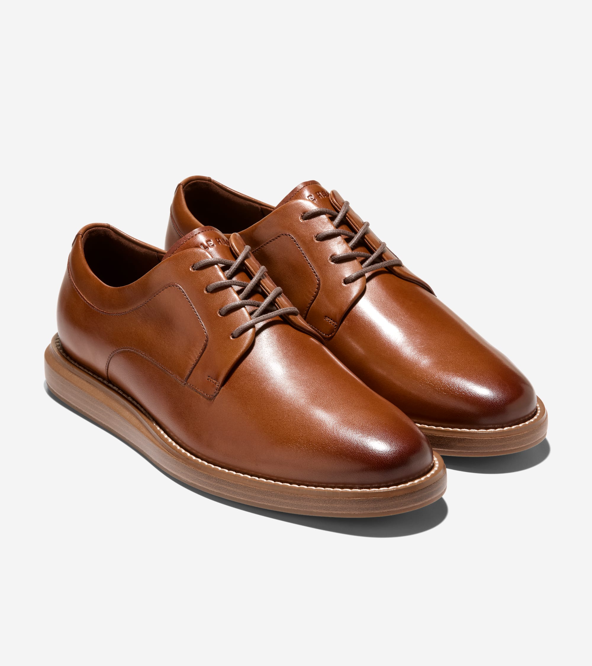 Pair of cognac brown leather plain toe oxfords with brown laces and thick tan soles with white stitching.