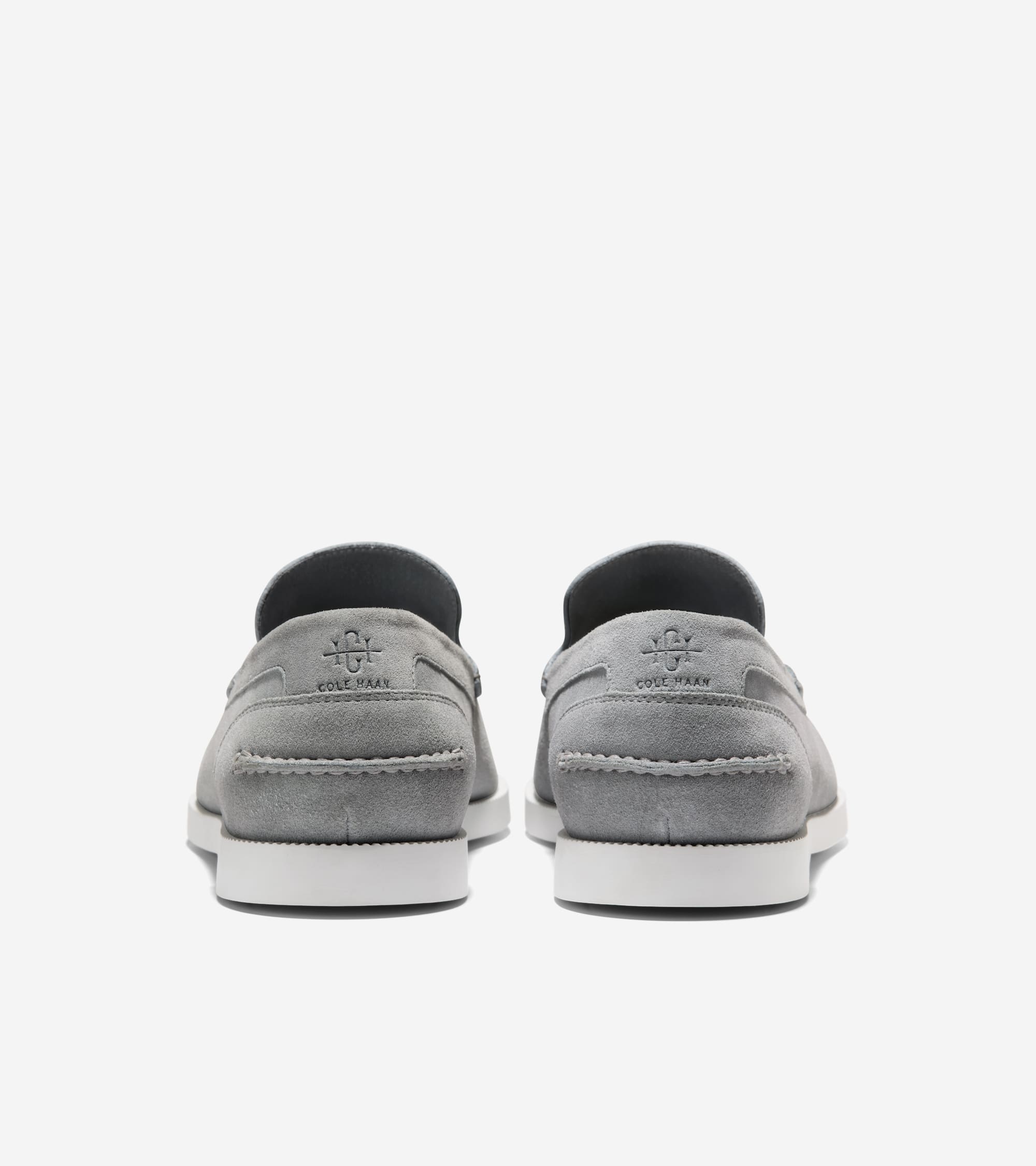 Pair of light gray suede loafers with white soles, featuring an embossed Cole Haan monogram and text on the back heel.