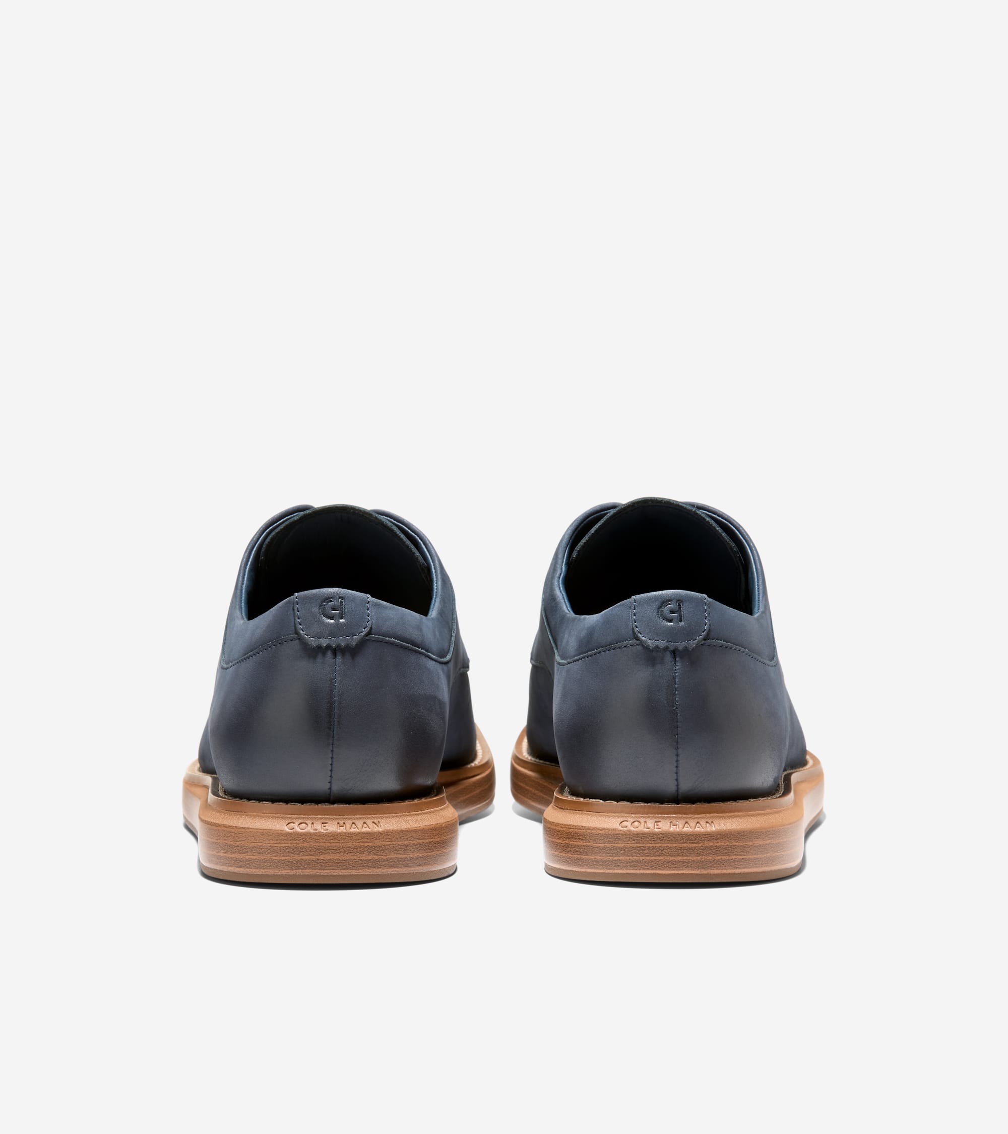 Dark blue matte leather oxfords, back view. Each has an embossed logo on the heel and a thick, tan sole with 'COLE HAAN' embo