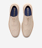 Light beige leather wingtip oxfords with brogue perforations, matching laces, dark blue insoles, and thick cream soles.