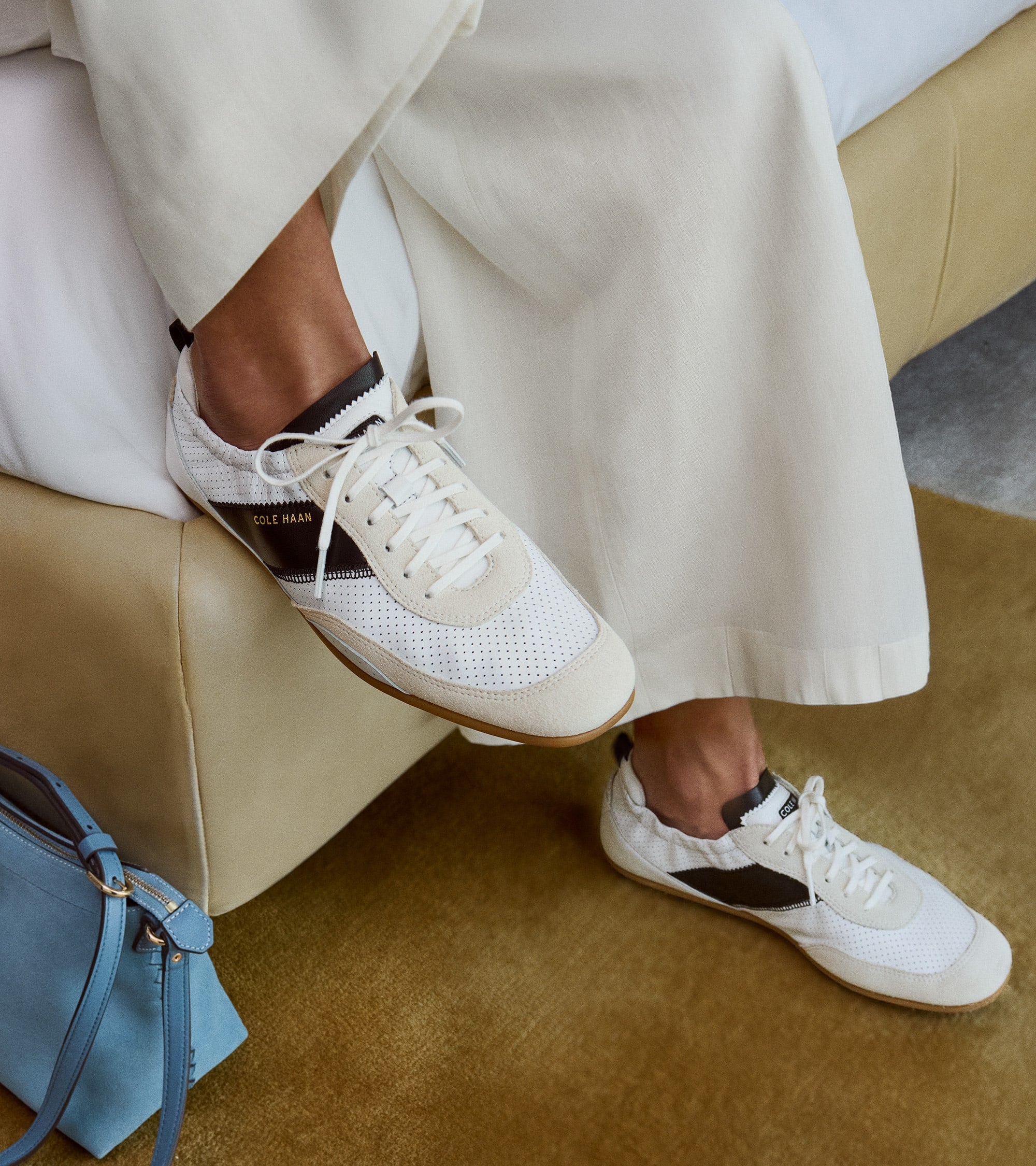 White perforated mesh sneakers with off-white suede accents, a black side stripe featuring gold-toned "COLE HAAN" text, and a