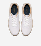 Pair of white leather low-top sneakers with white laces, tan soles, and tan collar trim. Dark blue insoles have gold-toned la