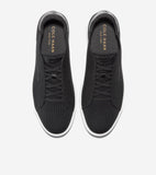 Pair of black knit slip-on sneakers with white soles, black elastic laces, and gold-toned Cole Haan branding on the insoles.