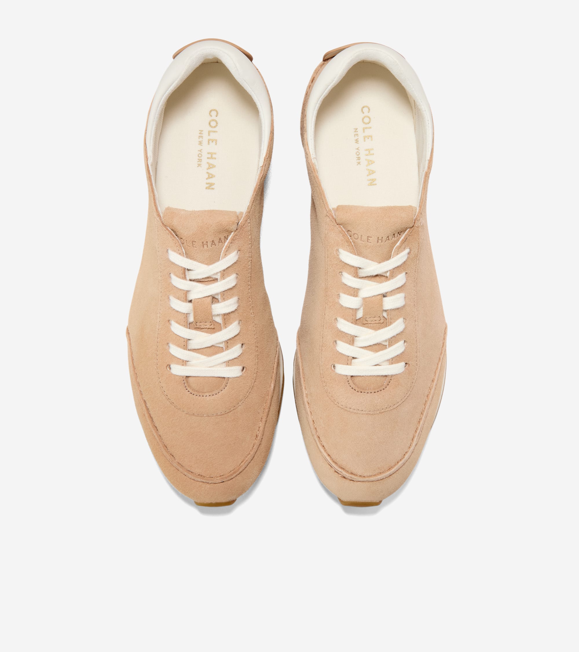 Pair of light tan suede low-profile sneakers with white laces and white interior lining. Gold-toned Cole Haan branding on ins