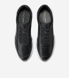 Pair of black slip-on sneakers with smooth uppers, elastic laces, embossed logo, white soles, and gold-toned Cole Haan brandi