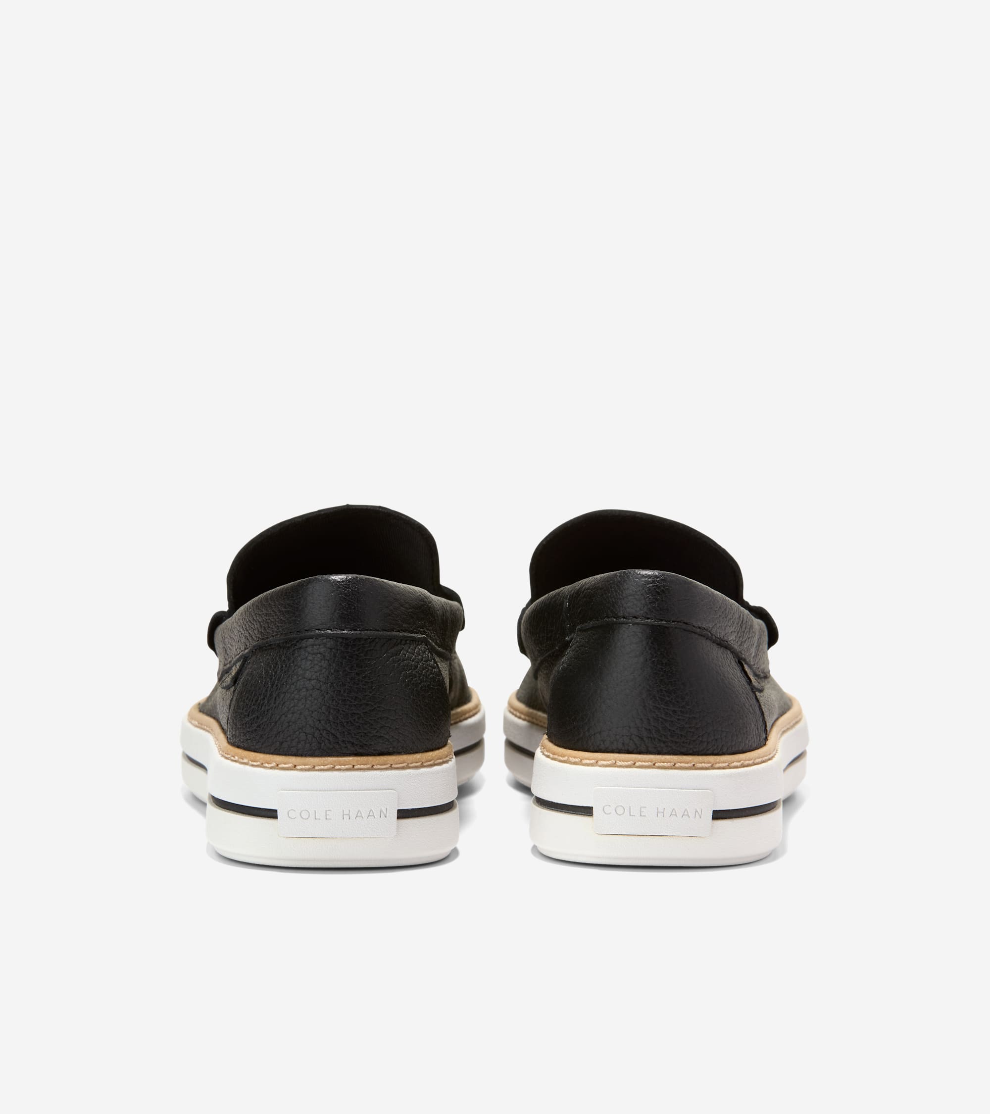 Black pebbled leather loafers with thick white platform soles, tan trim, and 'COLE HAAN' branding on the heel.