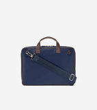 Navy blue slim briefcase with brown top handles and trim, a detachable navy fabric shoulder strap with silver-toned hardware.