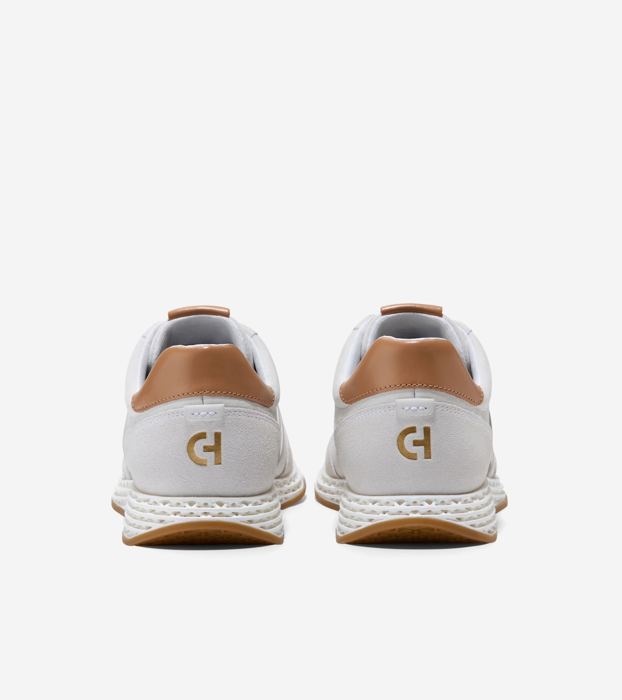Back view of two white sneakers with tan ankle collars, textured white soles, gum outsoles, and gold-toned CH logos on the he