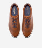 Pair of brown leather sneakers with laser-cut perforations, dark brown laces, white soles, dark brown ankle trim, and blue in