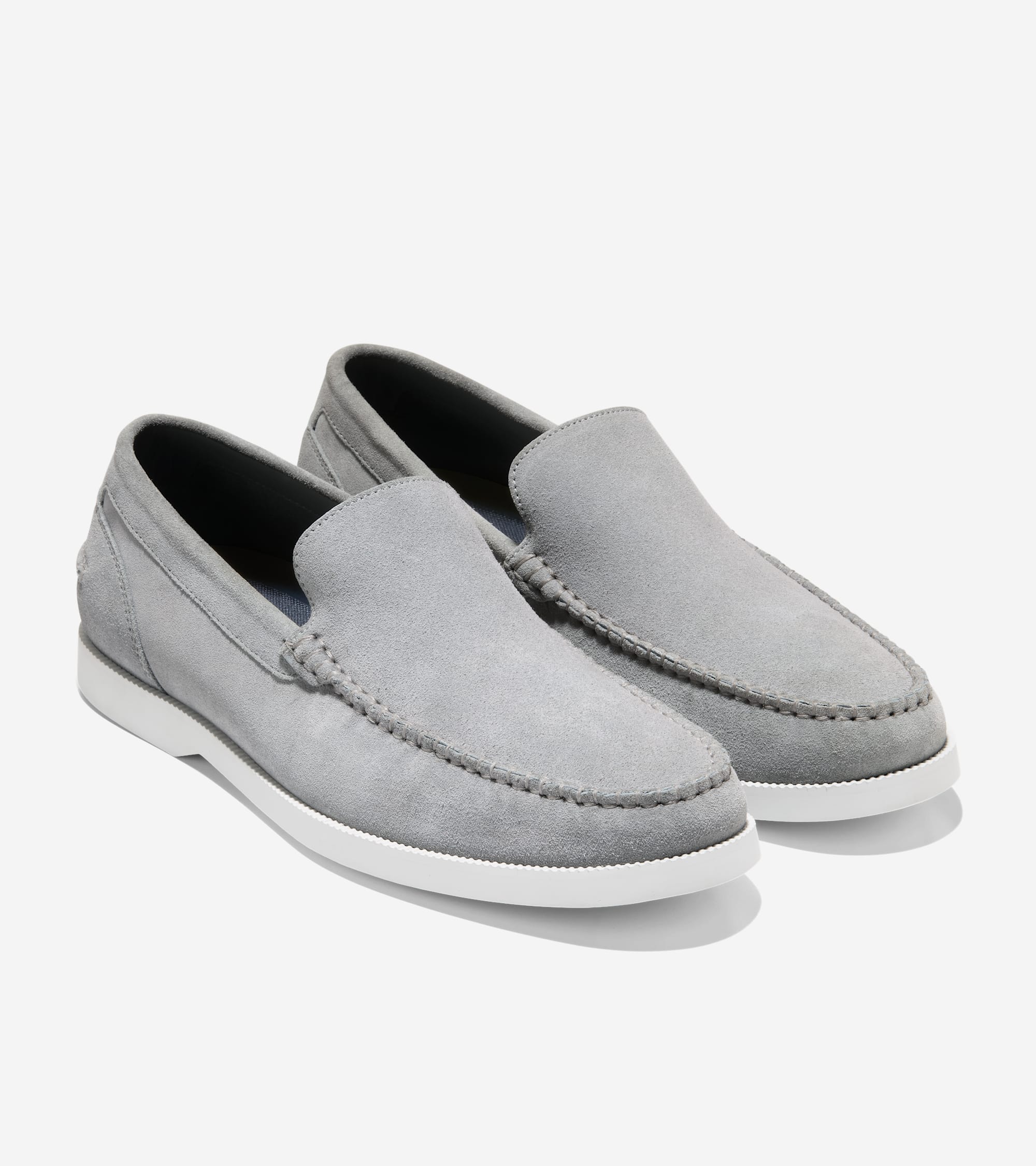 Pair of light gray suede slip-on loafers with moccasin-style stitching around the toe and white soles.