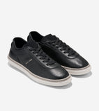 Pair of black pebbled leather low-top sneakers with black laces, white ridged soles, and light gray trim. Gold-toned 'COLE HA