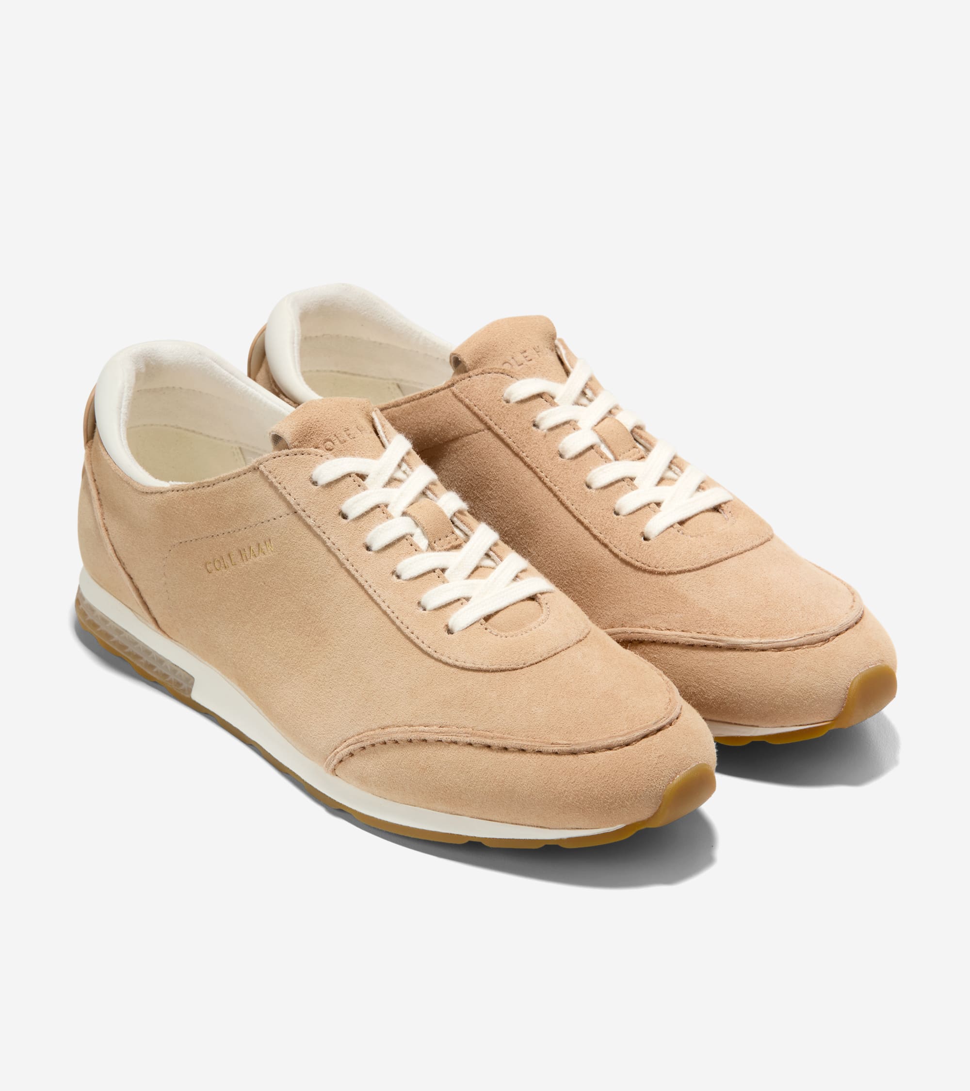 Pair of light tan suede low-profile sneakers with white laces, white midsole, brown outsoles, and translucent side detail.