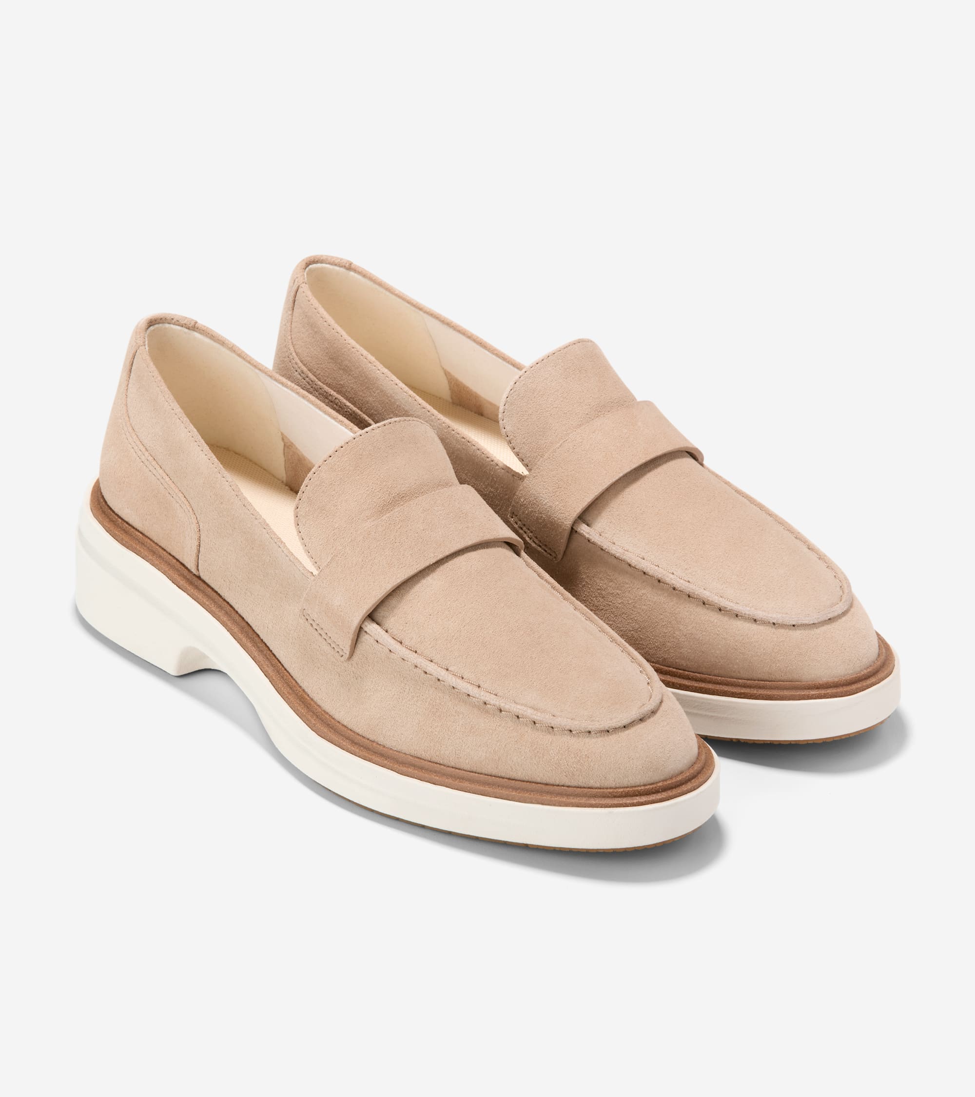 A pair of beige suede penny loafers with moccasin stitching, a brown welt, and a thick white sole.