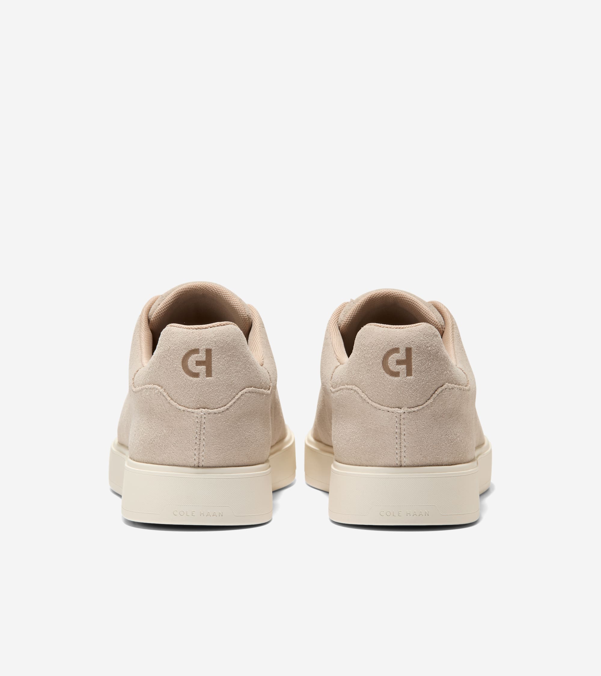 Pair of beige suede slip-on sneakers with thick cream soles. 'CH' logo on the heel and 'Cole Haan' on the sole.