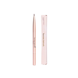 Bassam Fattouh Eyebrow Pencil in the shade Shadow, featuring a slim pinkish-gold dual-ended mechanical pencil body standing next to its minimalist light pink outer box packaging, available at blue salon.