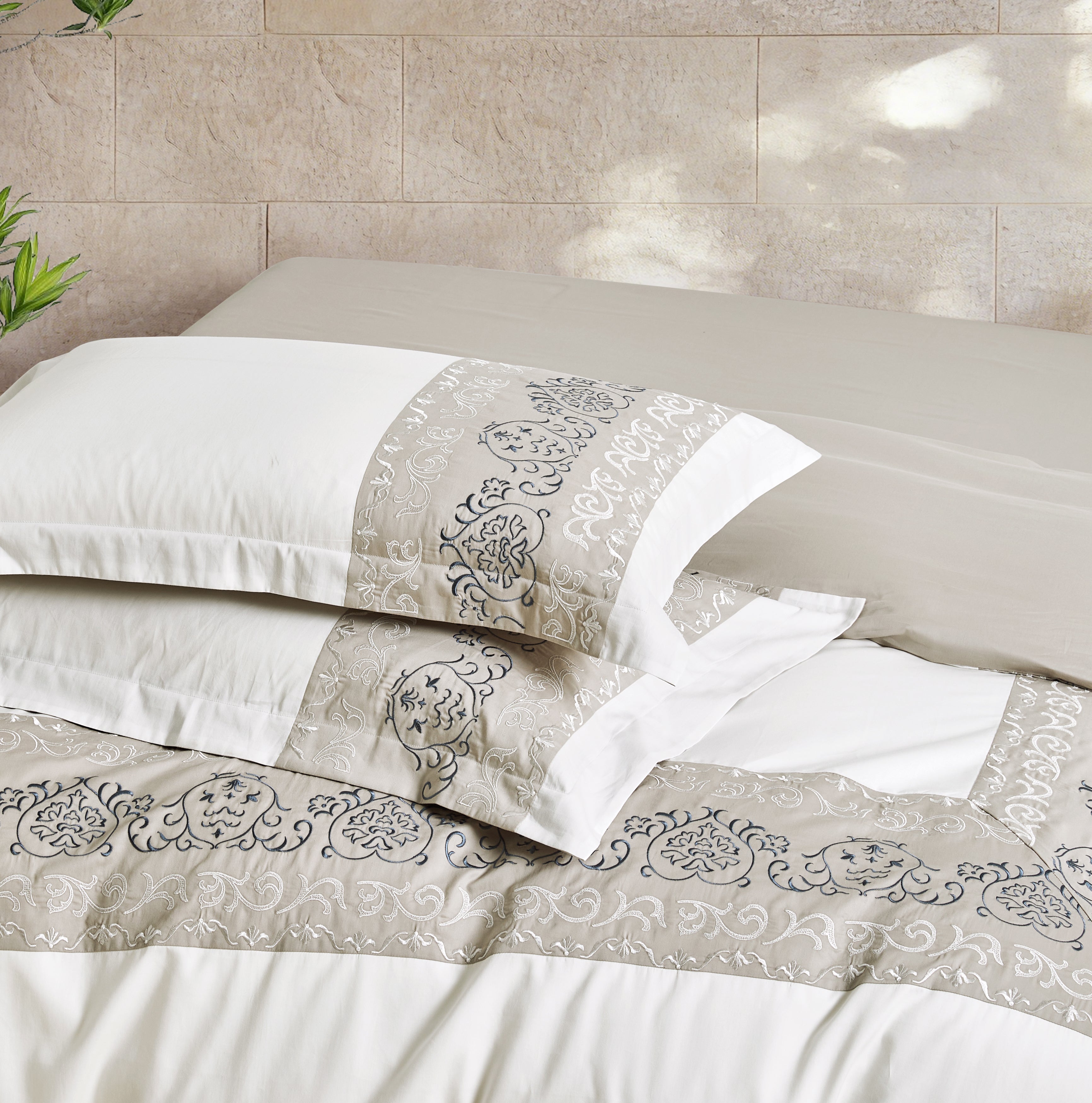 Stacked white pillowcases featuring elegant silver embroidered branch motifs.