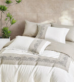 Close-up of intricate silver and grey vine embroidery on white luxury bedding.