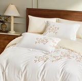 The soft white duvet is complemented by cream-colored sheets and shams, creating a layered, high-end neutral palette.