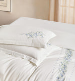 Detailed view of white pillowcases with vertical pink flower and leaf embroidery.