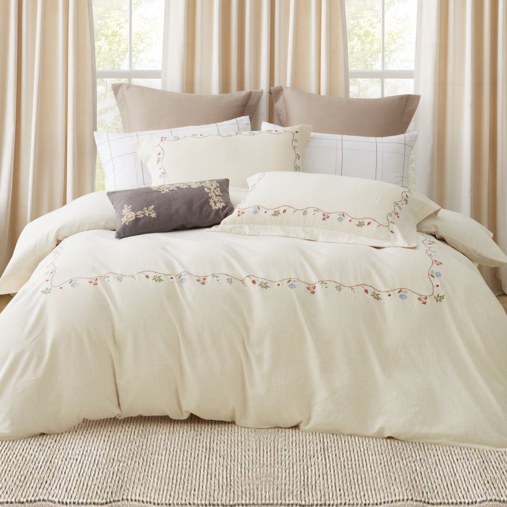 Full view of white luxury bedding with gold botanical vine embroidery in a warm bedroom setting.