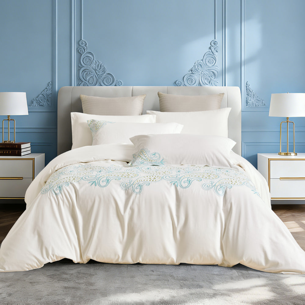 Frontal bedroom view of luxury white bedding with bright floral embroidery.