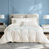 Frontal bedroom view of luxury white bedding with bright floral embroidery.