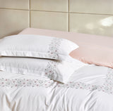 Angled view of a white duvet cover with a decorative embroidered botanical border.