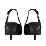 A pair of black slingback high-heeled sandals shown from the back, featuring a smooth black heel and sole with textured black fabric uppers and ankle straps, photographed on a solid white background.