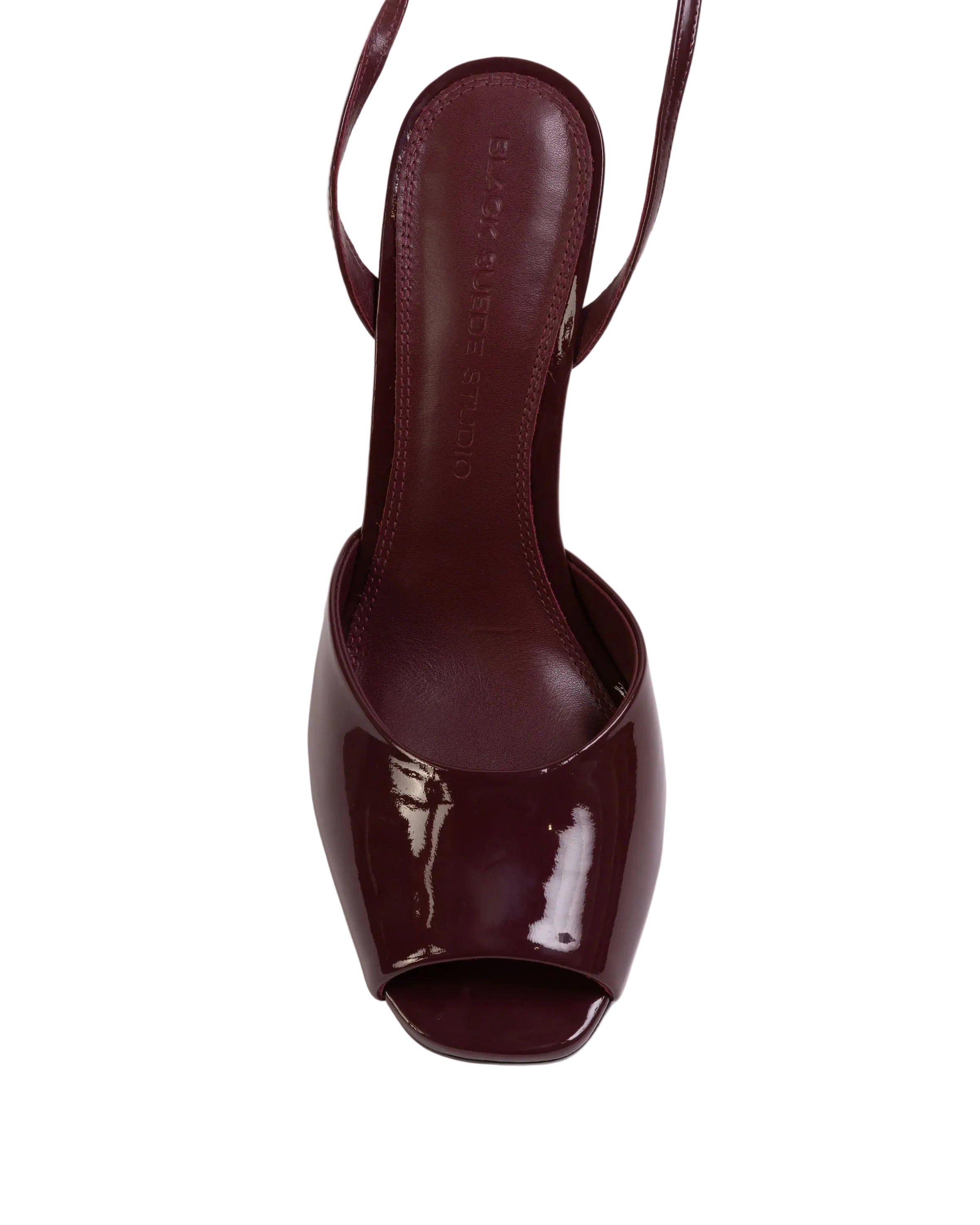 Overhead shot of a Black Suede Studio raisin patent leather wedge sandal showing the peep-toe design and the black leather insole with the brand name.