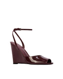Three-quarter view of an elegant raisin patent wedge heel against a neutral background, showcasing the peep-toe front and d'Orsay side styling.