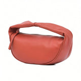 Three-quarter back view of the By Far crescent-shaped leather bag in burnt orange, showcasing its soft, slouchy padded handle at BLUE SALON.