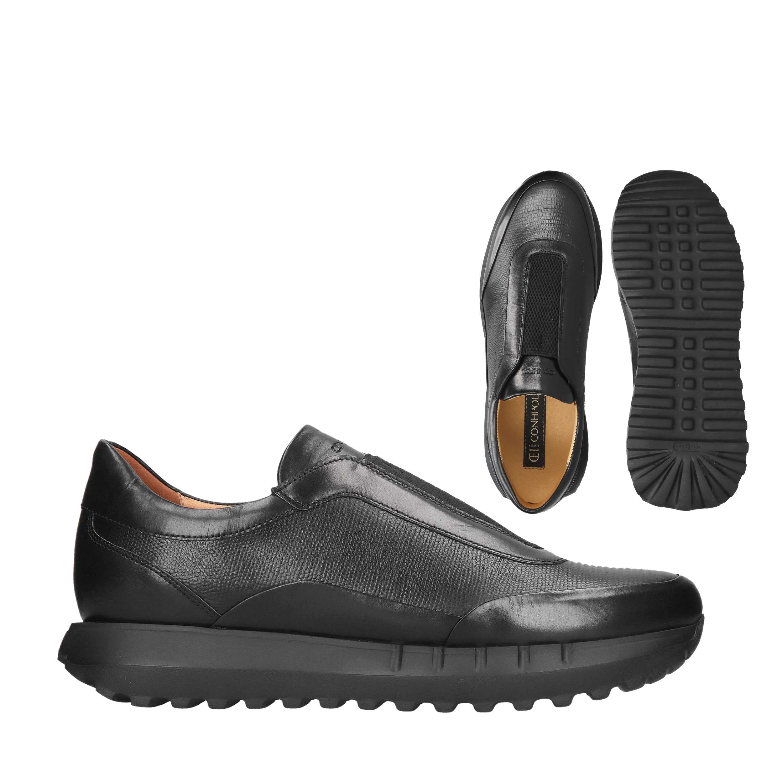 Black leather slip-on shoes with a textured vamp, smooth toe and heel, and a thick, ridged black sole. One shoe shows a tan i