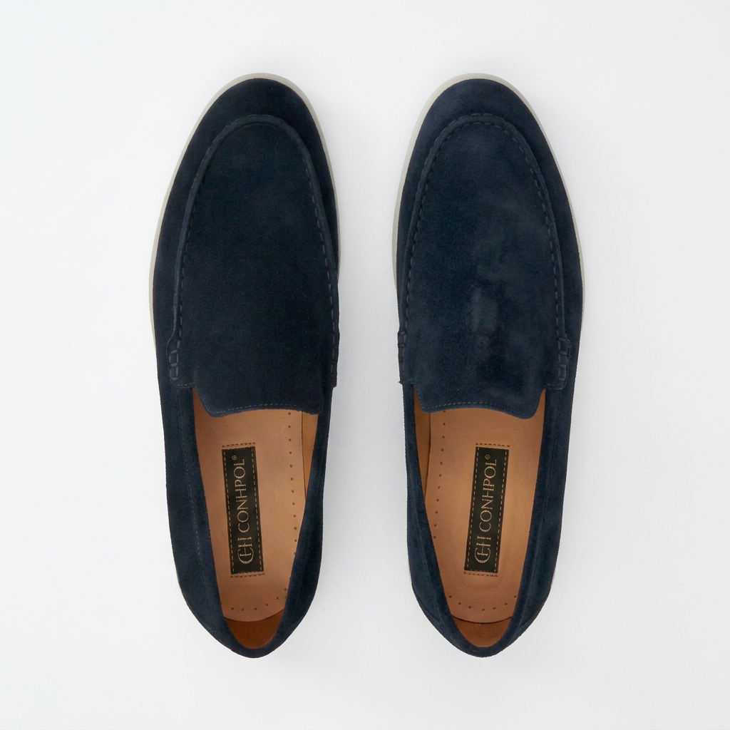 Pair of navy blue suede slip-on loafers with visible stitching around the toe box, light grey soles, and tan insoles.