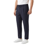 Three-quarter studio shot of a male model wearing the navy Eden Park pleated cargo trousers, demonstrating the side zipper utility compartment, styled with a white t-shirt and white low-top sneakers.