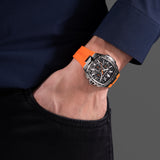 Silver-toned cushion-shaped watch with black textured dial, orange accents, three subdials, and an orange silicone strap.
