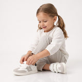 White and grey low-cut sneakers with two white velcro straps, a grey side stripe, and a "CK" logo. Black heel trim.