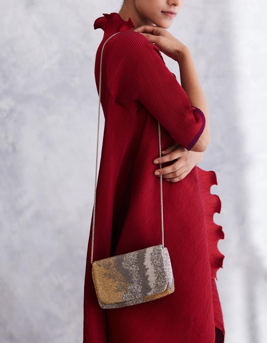Flapover clutch with a silver-toned chain strap, featuring a beaded pattern transitioning from gold-toned to silver-toned.