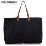 Black fabric tote bag with two brown leather-like shoulder straps attached by gold-toned rivets on brown oval patches. Top zi